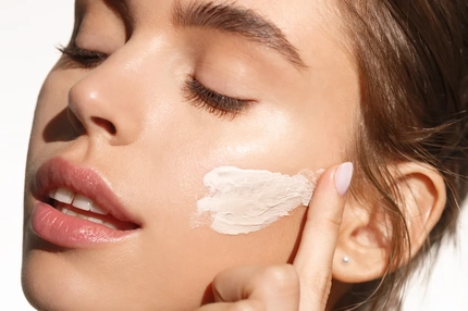 A woman swiping cream on her cheek.