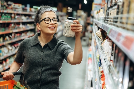 Middle-aged woman with short gray hair wearing glasses examines a jar of food.