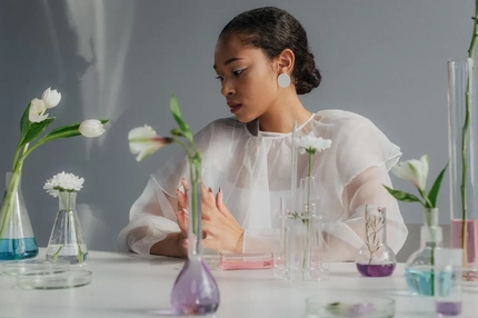 A woman with beakers and plants in front of her.