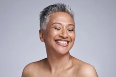 A woman with glowing skin smiles with her eyes closed.