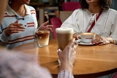 three friends drinking coffee in white mugs on a brown table