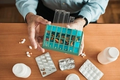 A hand holding a container of pills on a table full of pharma packaging