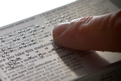 A finger touching the braille on a box of medicine