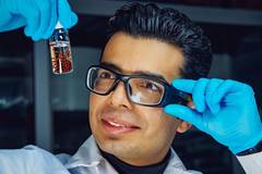 A person wearing glasses and gloves holding a small bottle