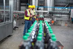 two factory workers monitoring cold drink bottle production