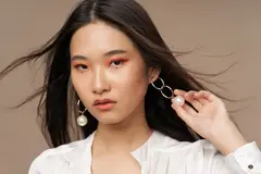 A woman wearing makeup and pulling at her earing.
