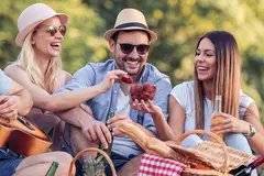 two young women and a man smiling and sharing strawberries in a park