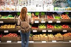 Woman standing in front of fresh fruit and vegetables shelves in the supermarket.