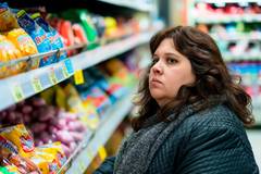 fat woman with an embarrassed look on her face in a supermarket in front of a shelf with sweets