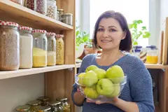 woman holds bowl of apples next to organized pantryw ith jars of grains