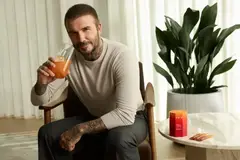 David Beckham sitting in a chair and preparing to drink an IM8 supplement.