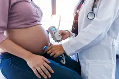 Obstetrician gynecologist performing Doppler auscultation checking blood flow in placenta and uterus in the clinic.