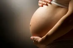 A pregnant women holding her tummy in a darkened room.