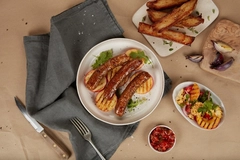 cultivated meat sausages on a white plate next to grey table cloth and dips