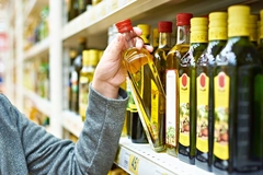 man's hand in grey sweater picking up olive oil bottle from supermarket shelf