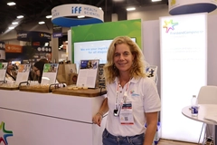 middle aged woman in white shirt standing at trade show booth