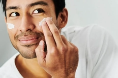 A man putting skin cream on his cheek.