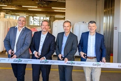 four men in suits cutting white ribbon inside factory