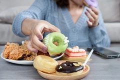 woman's hand reaches out for donuts on table full of junk food