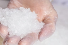 A hand in glove holding plastic granules.