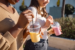 hands of two women walking with smoothie in transparent cups