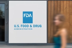 Image A woman blurry walking past a sign that says US Food and Drug Admiration.