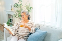 Happy Asian senior woman wearing glasses reading a book with drinking a cup of tea
