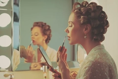 A woman wearing curlers putting on lipstick with a lip brush.