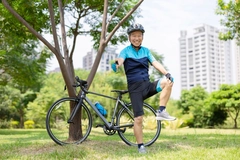 Man in biking gear in front of bike gives a thumbs up while touching his knee