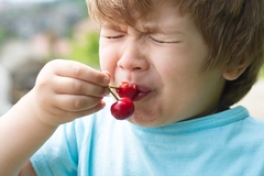boy eating cherries and making an unpleasant face