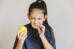 Image young girl in grey shirt eating lemon