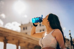 A woman drinks a supplement shake from a cup in the sun.