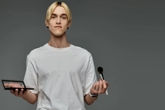Image A man holding a makeup palette and a makeup brush.