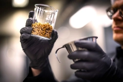 man wearing black gloves holding a glass jar of brown protein chunks