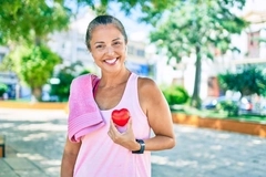 Image sportswoman in park smiling and holding heart object to chest