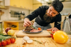 chef working in kitchen male chef decorating steak with rosemary leaf in kitchen