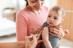 Image Doctor giving shot to little baby on arm, sitting on mothers lap