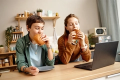 Image Gen Alpha children eating burgers looking at laptop screen.
