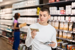 young man in white shirt looking at two protein bars in supermarket