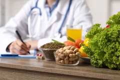 Young female nutritionist with clipboard and healthy food writing diet plan in office