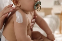 Image Baby with pacifier being moisturized on arm
