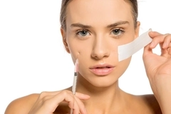 A woman holding a needle and tape to her face.
