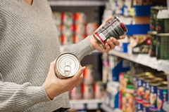 Image Woman holding two cans reading label in grocery store