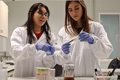 Image two women in lab gear checking liquid in vial