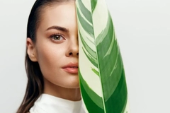 A woman with a leaf in front of her face.