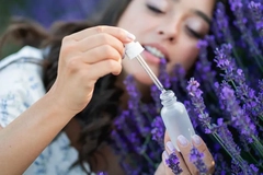 A woman sitting in lavender flowers holding a bottle of serum.