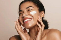 A woman putting lotion on her face and smiling.