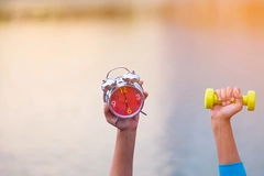 Image two arms up, one holds alarm clock another holds weights