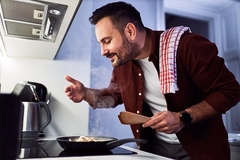 Image A man enjoying the aroma of his meal in a pan, cooking in his kitchen.