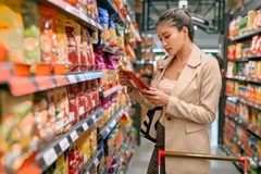 A woman studies the labels on a snack in a grocery store.